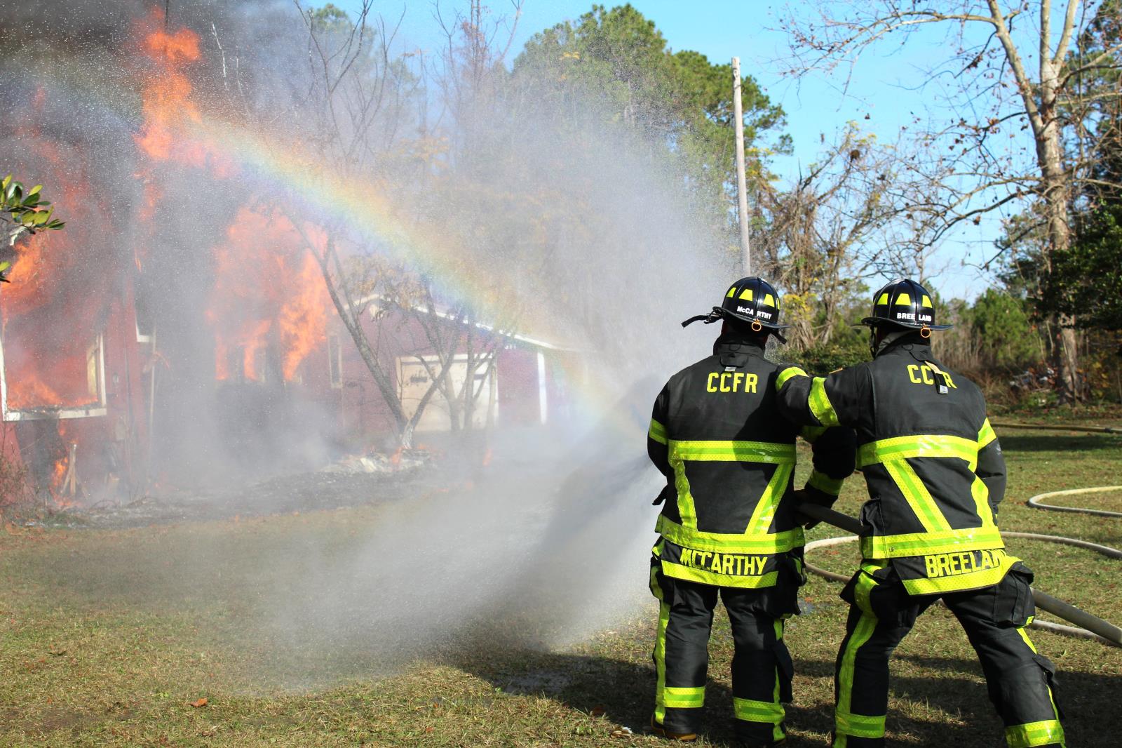 Two firefighters using the firehose to put out a fire with rainbow in the water