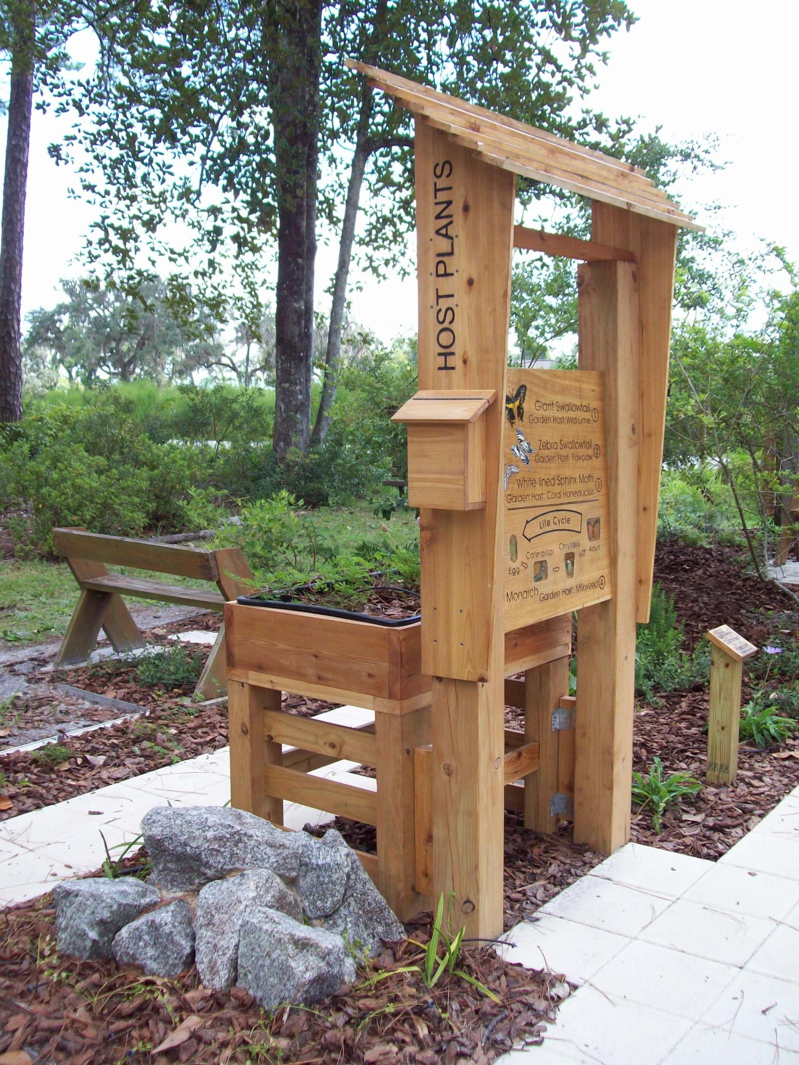 Pollinator kiosk with a bench, rock, sidewalk, and raised flower bed