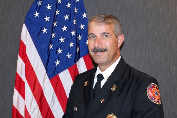 Headshot of Chief Motes posed in front of a flag