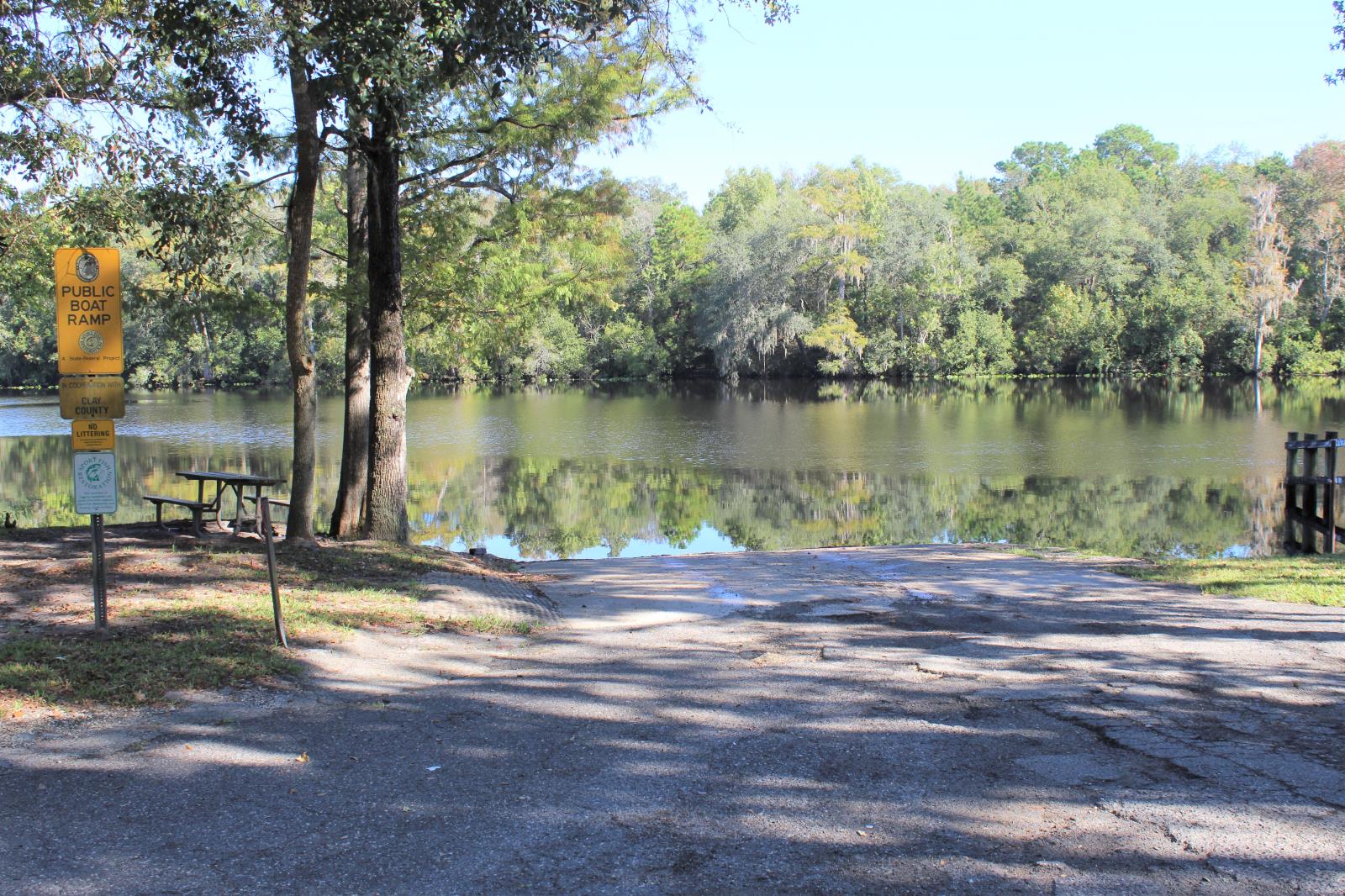 Boat ramp leading to the creek with a picnic table to the left under trees