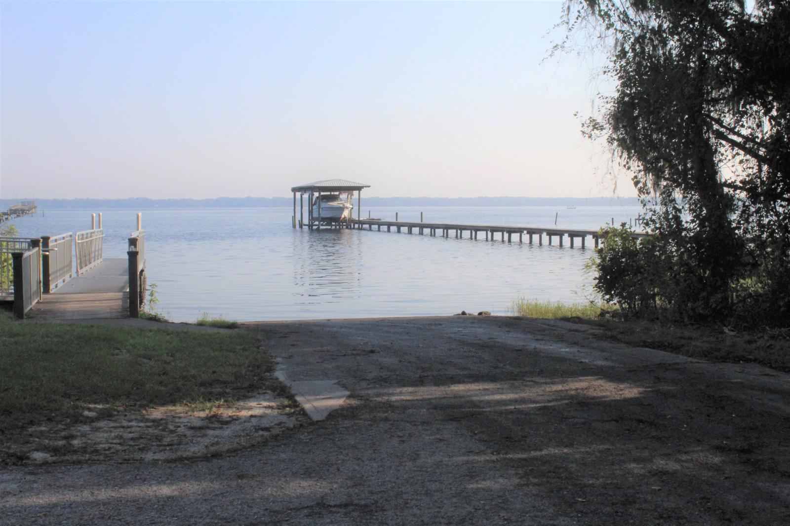 Paved boat ramp leading to the river with a boat dock to the left and a boat in a dry dock