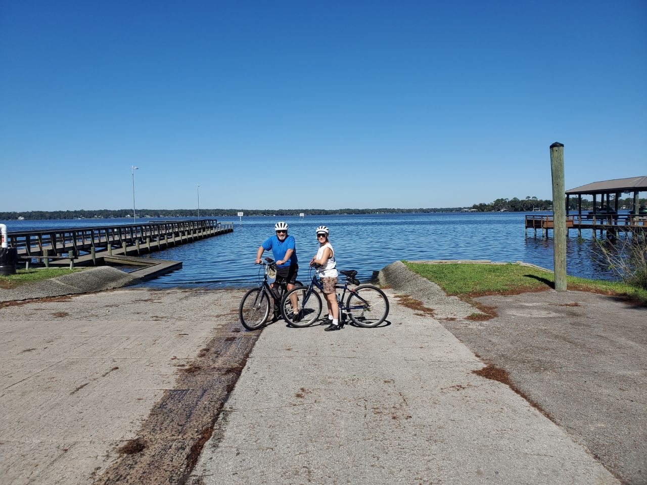 Couple posing on their bicycles wearing helmets in front of the river on the boat ramp leading to the water