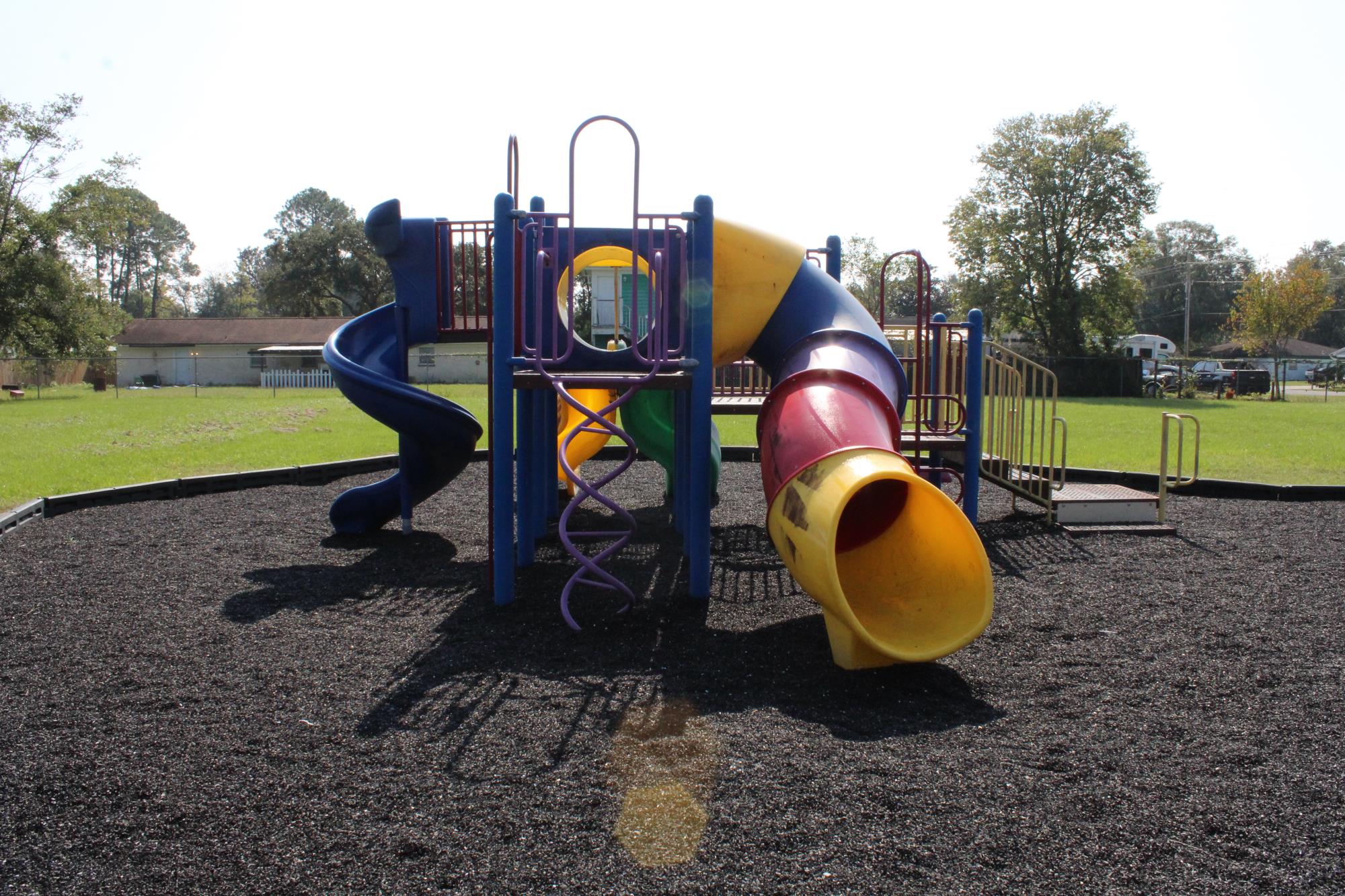 playground equipment with a yellow slide in the shredded rubber tire with sun spots in the photo