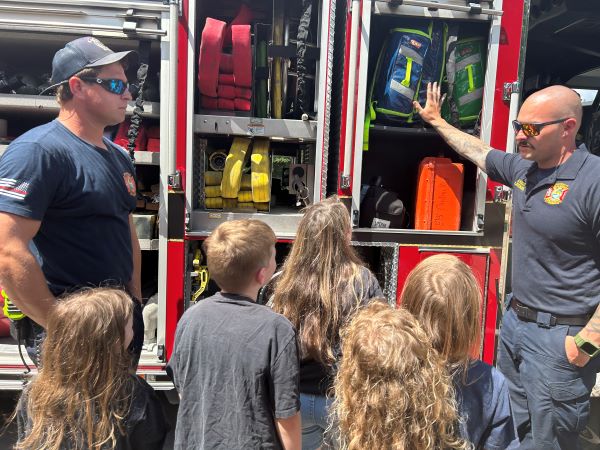 Two firefighters showing children a fire truck