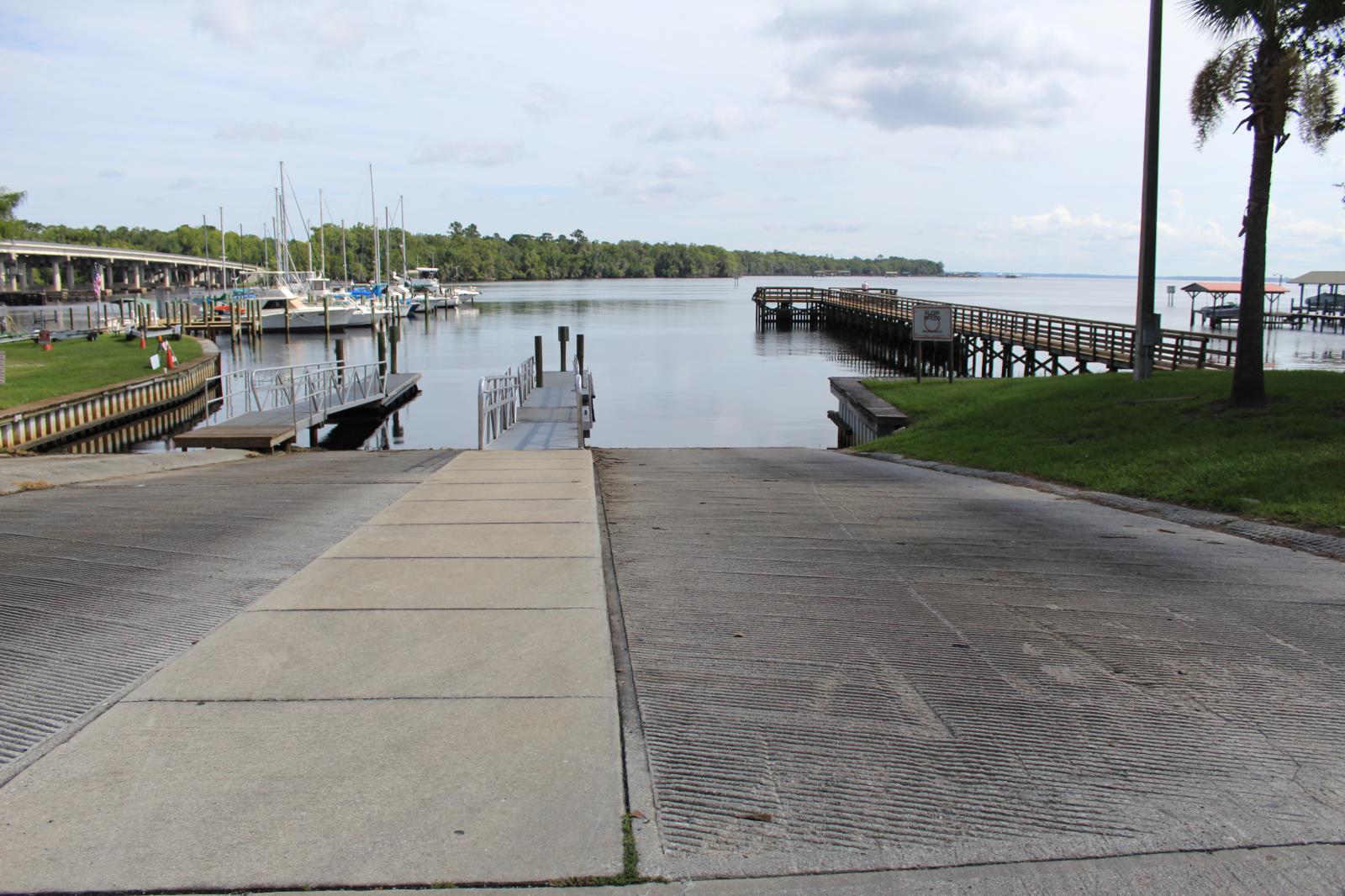 Paved boat ramp leading to the water with a wooden dock to the right and a boat dock to the left